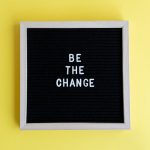 Minimalist letter board with 'Be The Change' quote on a vibrant yellow background.